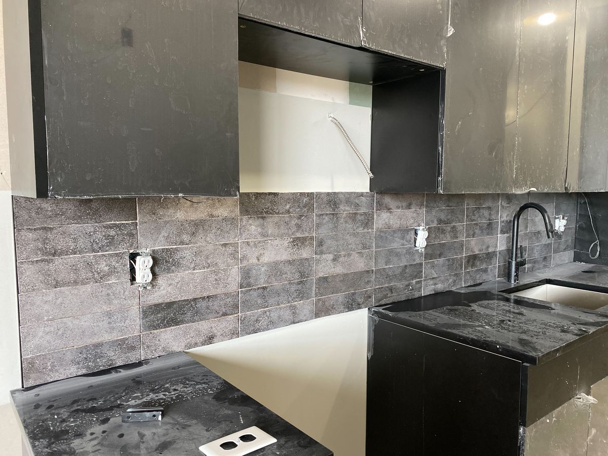 Close-up of dark slab cabinets, quartz counter, and tiled backsplash in an apartment kitchen install